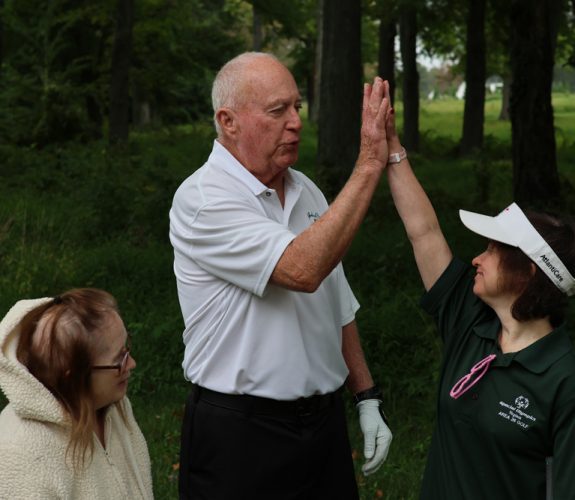 Golfer (center) high fiving a Gabriel Homes resident (right).