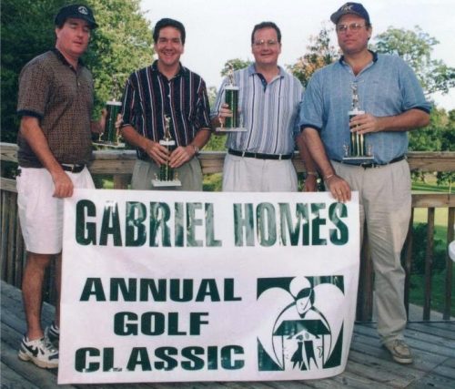 Golfers with trophies and a banner at the Gabriel Homes Golf Tournament.